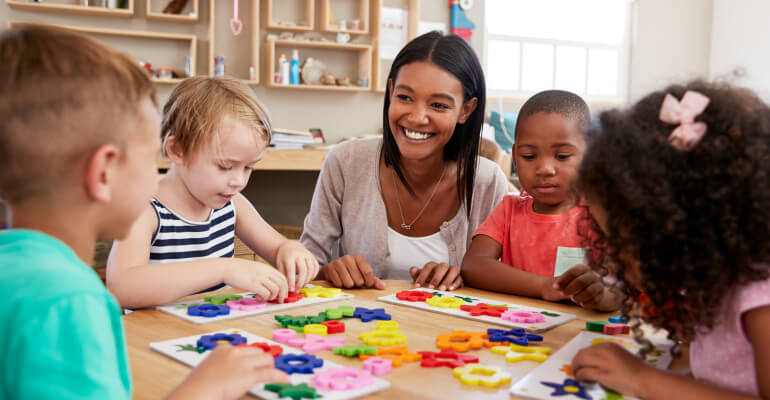 Female teacher sits with four elementary school age children as they work with hands-on shapes.