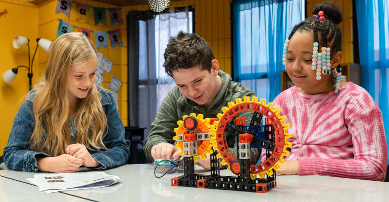 Three students work on a compound machines STEM lesson from Kid Spark Education.