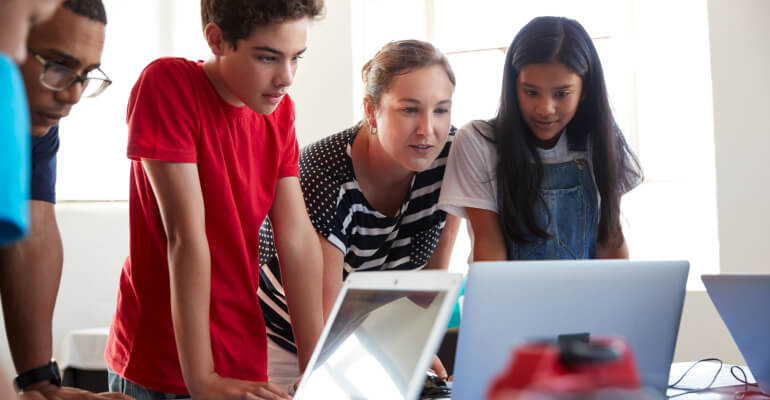 Teacher and two students in front of a laptop, working together on a task.