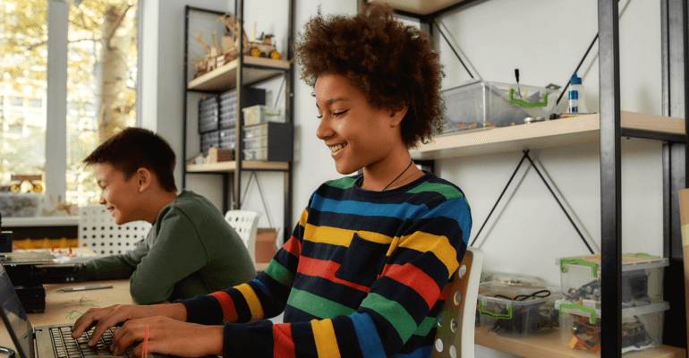 Two middle school aged male students smile as they work on laptops.